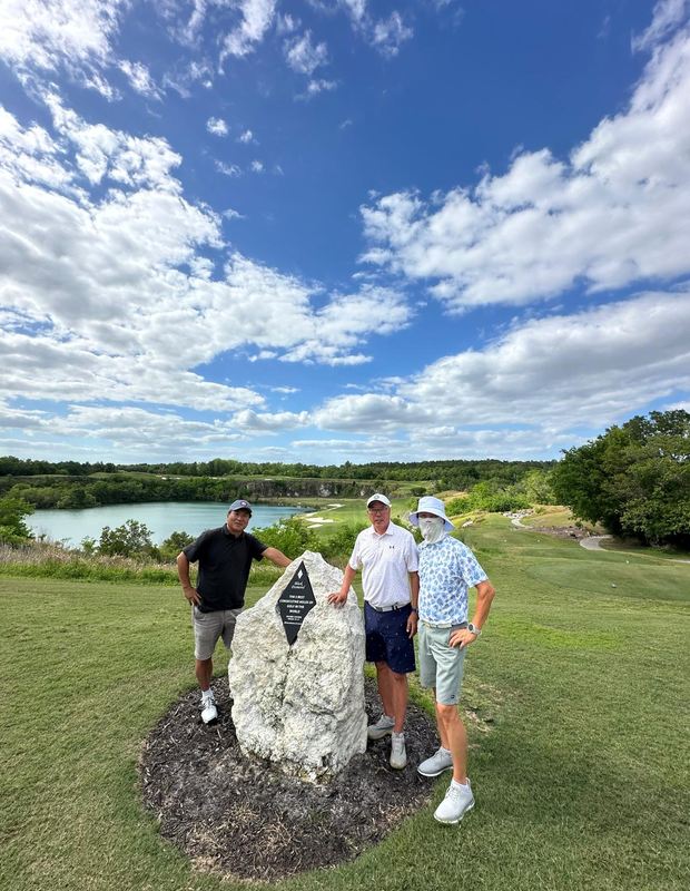 'THE 5 BEST CONSECUTIVE HOLES OF GOLF IN THE WORLD'이라 새겨진 표지석 앞에 선 세 사람